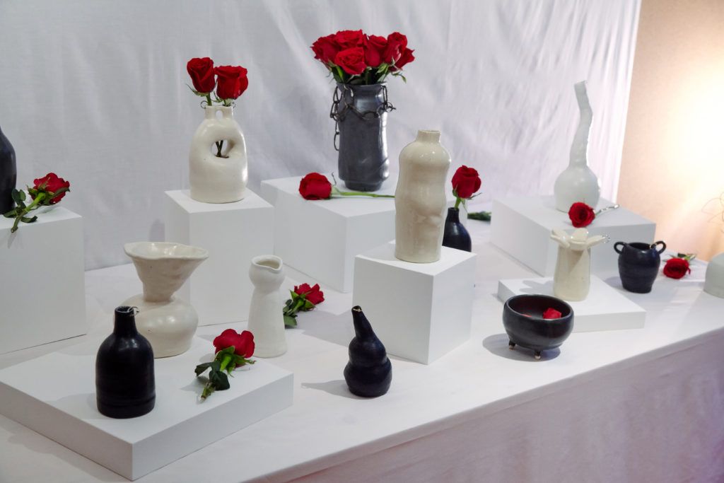 A white-clothed table with multiple ceramics in black and white scattered about with red roses.