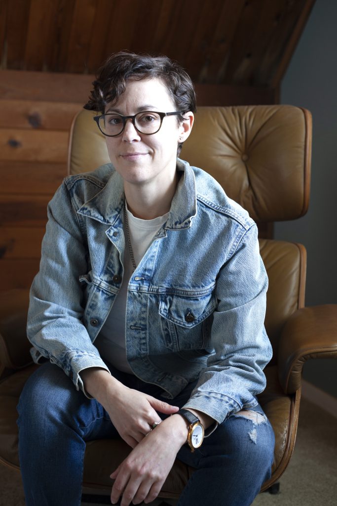 Casey Parks sitting on brown leather chair in stone-washed denim jacket.