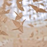 Dozens of white paper cranes look as if they are flying across image