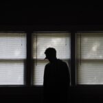 Silhouette of guy in front of window shades.