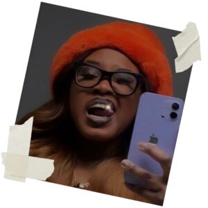 Ashely Tate, a Black woman, showing off her grill. She's wearing a red fuzzy hat and holding a purple phone.