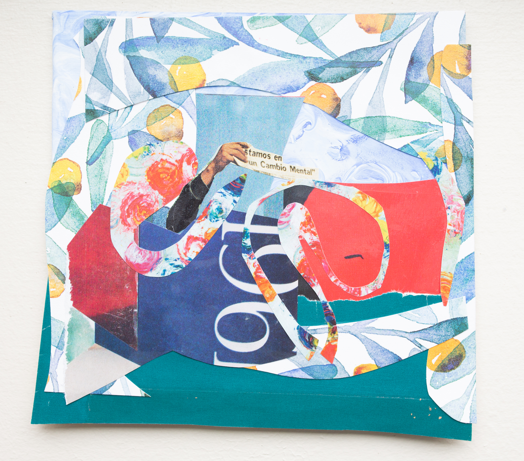 A collage of flowered wall patterns with blue-green leaves and yellow balls, mixed with colored, torn paper in the center, from which a hand emerges with the words "estamos en un cambio Mental."