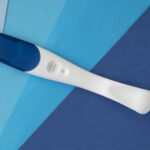 Pregnancy test with a blue cap on a background of various blue triangles.