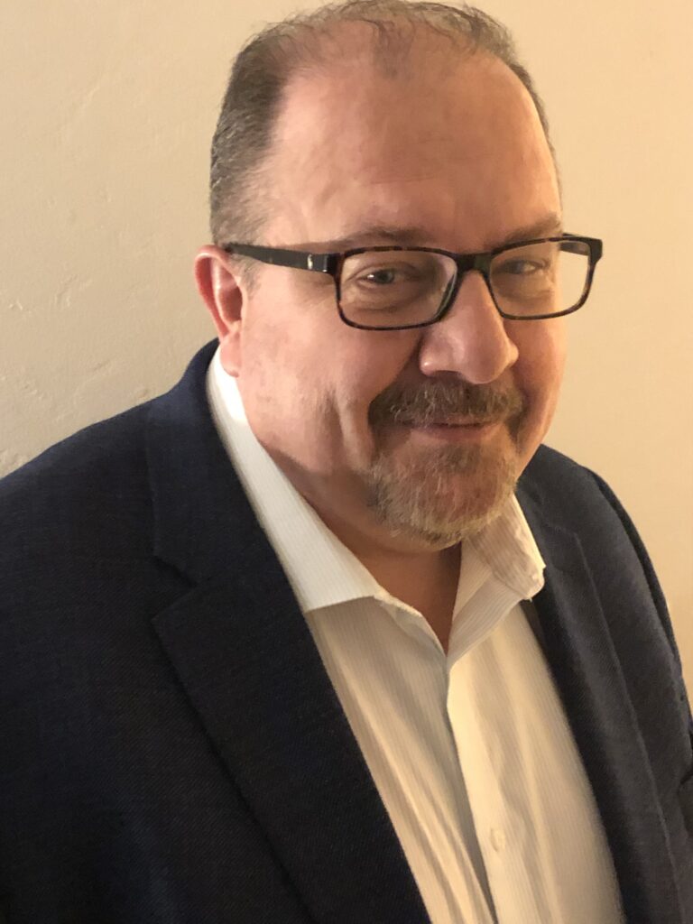 White man with brown glasses, graying hair and facial hair.