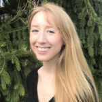 Amanda Hodes in a black shirt in front of pine trees.