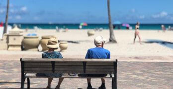 Two elderly people on a bench overlooking a beach.