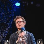 Mark Tardi, man with microphone in front of black background.