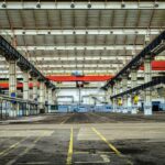 The inside of a warehouse factory with red and blue beams is shown. It looks vast and empty.