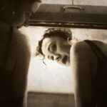 Two women in makeup look back from a lid.