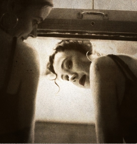 Two women in makeup look back from a lid. 