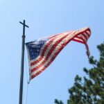 An American flag on a pole topped with a Christian cross, viewed from below