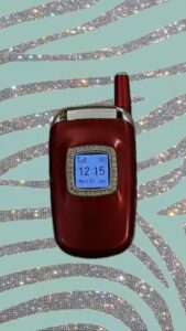 A closed, red flip phone on a table and displaying the time 12:15